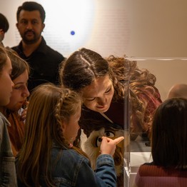 Bild einer Vermittlerin, die Kindern etwas in einer Glasvitrine zeigt.