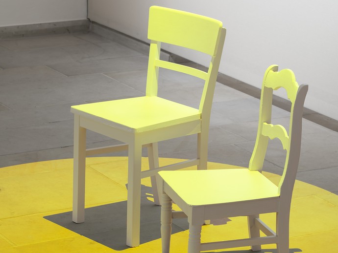 Eindruck der Ausstellungsgestaltung: ein kleiner Stuhl in einem gelben Farbkreis im Raum "Spotten". (öffnet vergrößerte Bildansicht)