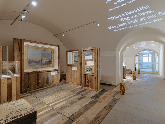 Zu sehen ist ein Blick in die Ausstellung mit verschiedenen mit Holz verkleideten Vitrinen. (vergrößerte Bildansicht wird geöffnet)